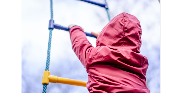 a child in a red jacket climbing a rope ladder